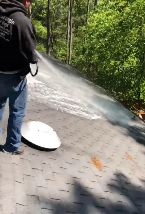 Technician in a West Georgia Gutter Guys hoodie soft washing a shingle roof, spray fanning out